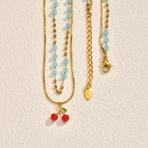 Collana a doppio strato dorata con ciondolo a ciliegia e perle azzurre su fondo bianco