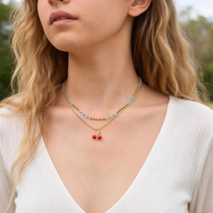 Dettaglio della collana a strati con ciliegia su modella con perle blu e catena d'oro