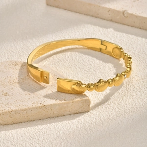 Détail d'un bracelet doré avec relief de coquillage et fermoir ouvert sur pierre
