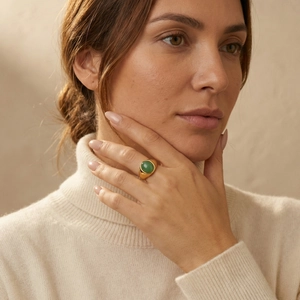 Dettaglio di un anello a sigillo dorato con gemma verde sul dito della modella