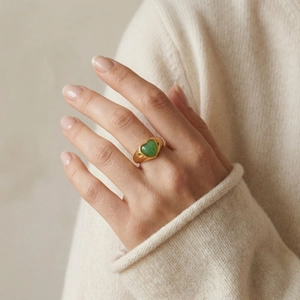 Dettaglio di un anello a cuore dorato con pietra aventurina verde e un maglione di maglia