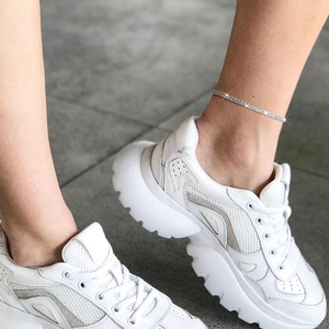 Detailed view of a sparkling crystal anklet chain worn with white platform sneakers