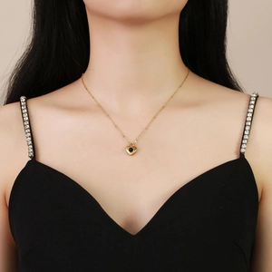 Detail van de gouden hartjesketting met zwarte kraal gedragen door model in zwarte jurk