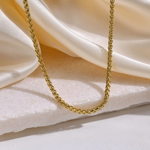 Detalle macro de collar de cadena dorada sobre piedra de mármol y tela de seda crema