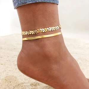 Gold stainless steel snake and chevron anklet set worn by model on sandy beach