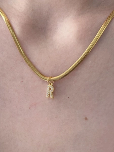 Dettaglio collana catena a serpente dorata con ciondolo lettera R e zirconi indossata