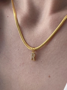 Dettaglio collana a catena serpente dorata con ciondolo a lettera R in pavé di cristalli