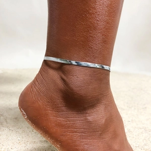 Detailed close-up of a silver herringbone snake chain anklet on a tanned ankle at the beach