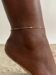 Golden snake chain anklet with oval textured charms worn on ankle for a stylish look