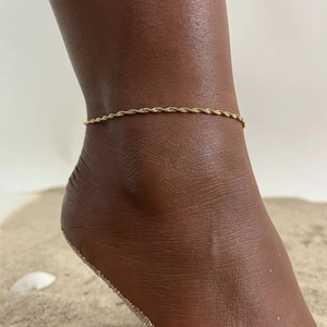 Detail of a golden twisted rope anklet worn on the beach with sea shells and fine sand