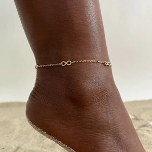Detail of gold infinity charm anklet on dark skin at beach with summer vibes