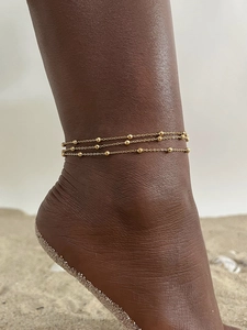 Close-up of triple layered gold bead anklets on woman's ankle at the beach