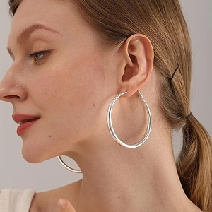 Detailopname van grote zilveren oorringen op model met een minimalistisch metalen design