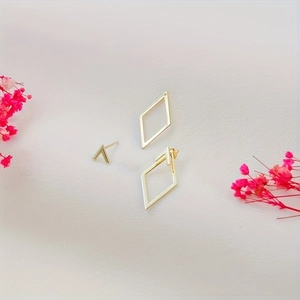 Macro detail of geometric gold rhombus earrings and V-studs on white fabric background