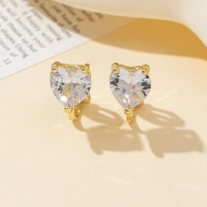 Dettaglio di orecchini a cuore in zircone con griffe placcate oro su sfondo beige