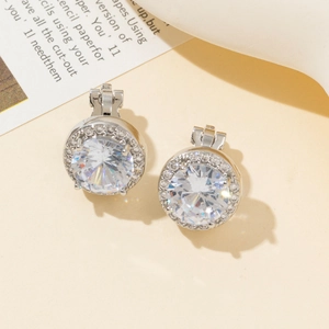 Dettaglio di orecchini halo in argento con zirconi rotondi su uno sfondo beige caldo