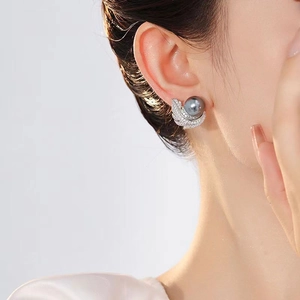 Detail of a grey pearl stud earring with silver feather setting worn by a model