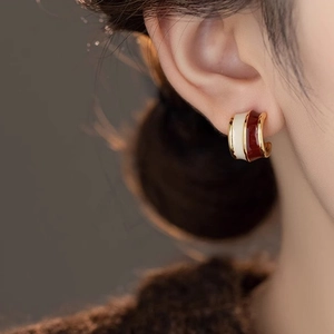 Close-up of vintage C-shaped gold-plated hoop earrings with cream and deep red enamel