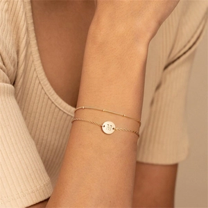 Detail of a layered gold bracelet with a round charm featuring the engraved letter M