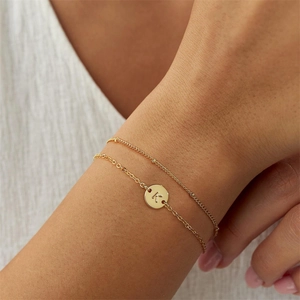 Detail of a gold-plated double-layer bracelet with a round letter K pendant on a wrist