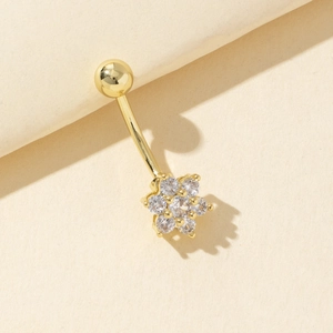 Piercing de ombligo floral dorado con piedras de circonita sobre fondo beige