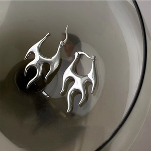 Silver flame hoop earrings with bold metal design in a stylish glass container