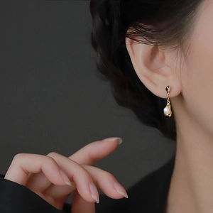 Dettaglio di orecchini a pendolo in oro con perla indossati da una modella