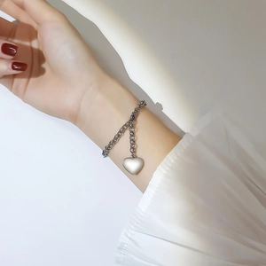 Bracelet avec pendentif coeur argenté porté au poignet d'une femme avec chaîne épaisse