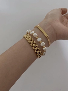 Close-up of stacked gold chain bracelets with baroque pearls and rectangular blank tag