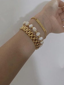 Close-up of layered gold chain bracelet, rectangular plate, and elegant pearl strand