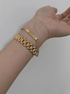 Close-up of gold chain bracelets with a rectangular blank metal plate on a woman's wrist