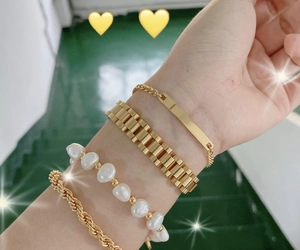 Close-up of four stacked gold-tone bracelets featuring chain, pearl, and plate details