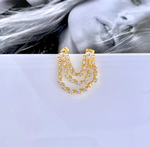 Detailed view of gold triple-layer tassel earrings with white zircon on a minimal background