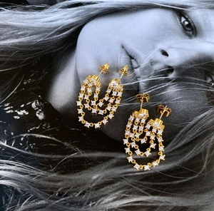 Macro detail of gold-plated tassel earrings with three-layer chains and white zircons