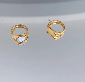 Detailed top view of gold signet rings with one mother of pearl inlay on gray reflective surface