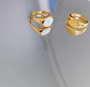 Macro detail of gold signet rings with white seashell inlay on a reflective surface