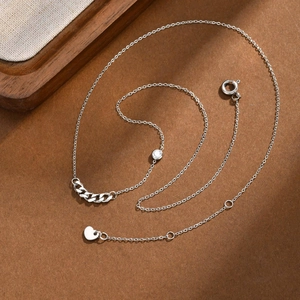 Detail view of silver chain necklace featuring round zircon and heart pendant on wood surface