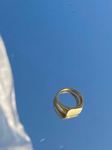 Polished gold signet ring with flat top surface reflected on a clear blue sky mirror