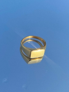 Macro shot of polished gold seal ring with flat rectangular top on blue mirror surface