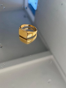 Close-up of a polished gold signet ring reflecting on a grey surface with water drops