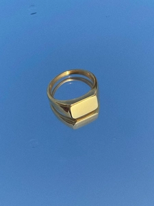 Macro detail of polished gold signet ring with rectangular face on blue reflective surface