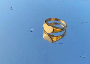 Macro detail of a heart-shaped polished gold ring reflecting on a blue water surface