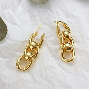 Close-up of chunky gold chain link earrings on a minimalist white textured background