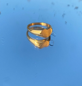 Macro shot of a golden heart signet ring reflecting on a blue water mirror surface