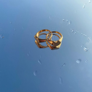 Pair of polished gold heart signet rings on a reflective blue surface with water drops