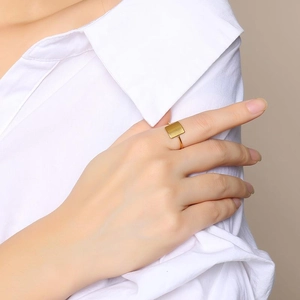 Anello a sigillo quadrato dorato lucido indossato con una camicia bianca minimal
