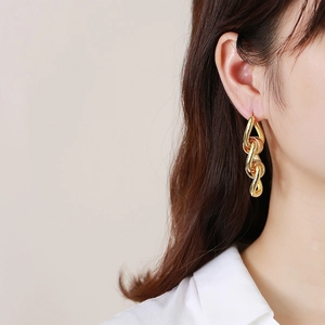 Close-up of gold tone triple link chain dangle earrings worn by a female model