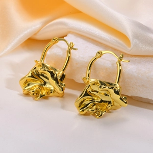 Detailed view of gold twisted square earrings on elegant cream satin and stone base