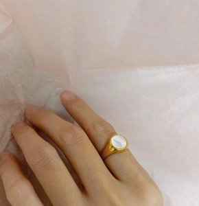 Detailed view of a gold signet ring with a round white shell inlay on model's finger