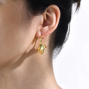 Close-up of golden irregular lava texture drop earrings worn on ear for detail